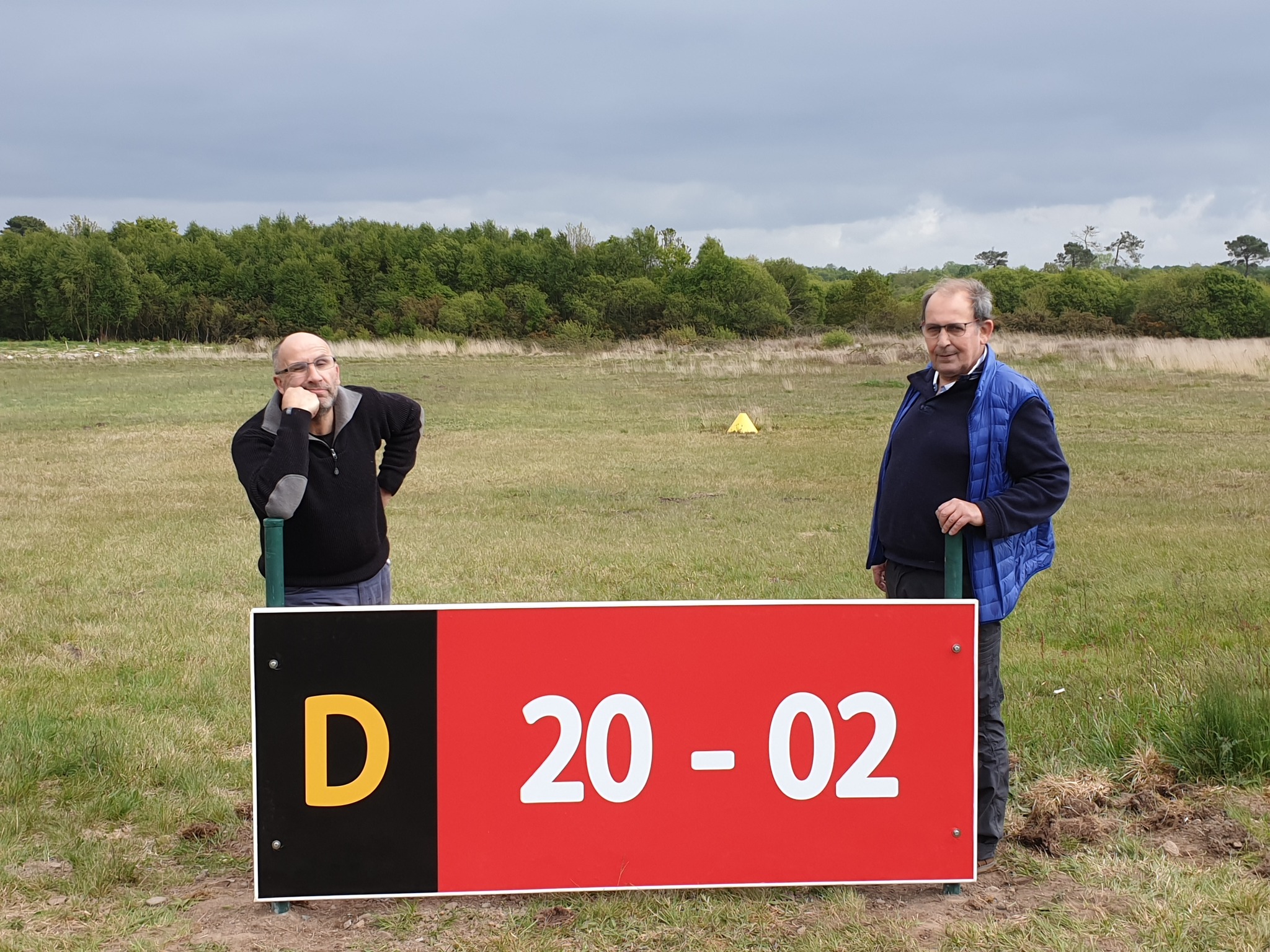 Deux bénévoles de l’Aérodrome Bretagne Atlantique posant à côté d’un panneau de signalisation de piste.